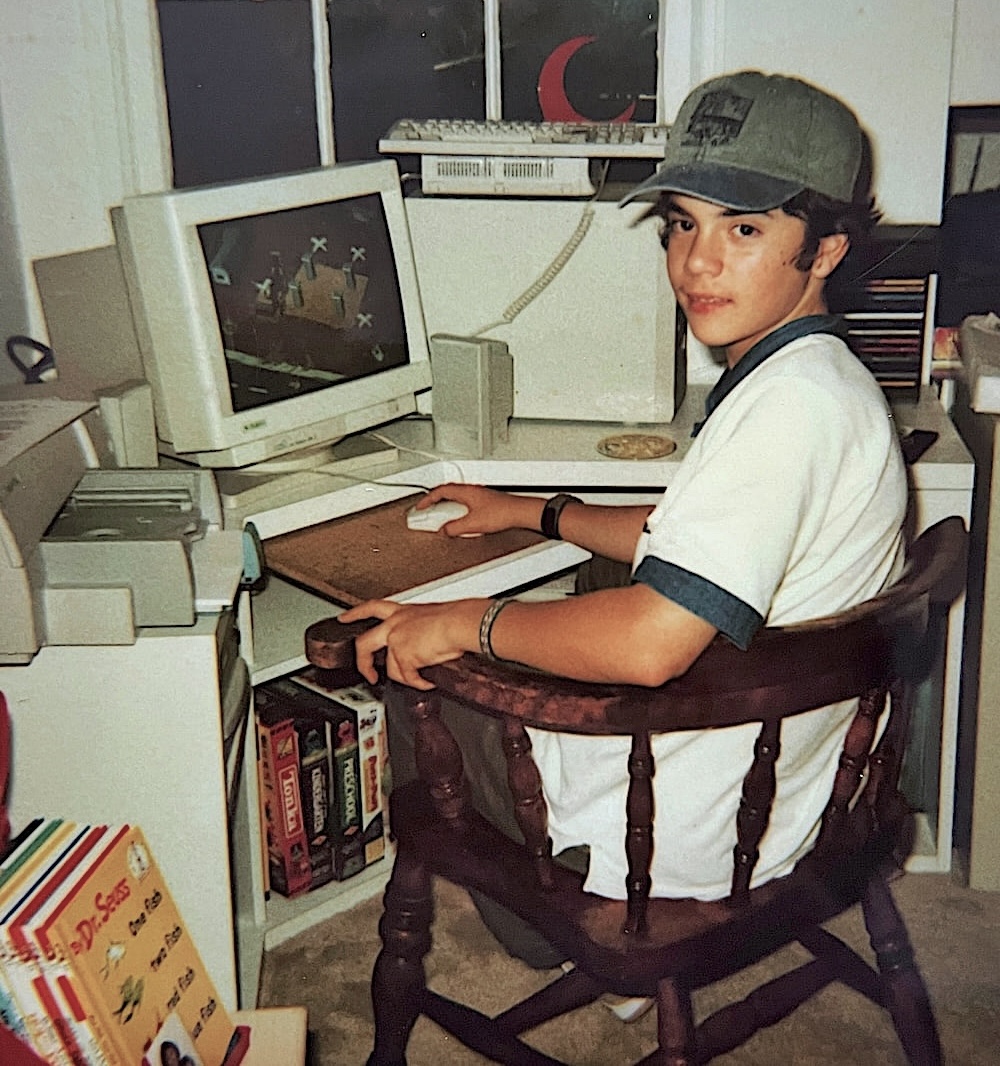 Fotografía de un pequeño Carlos frente a un computador, sonriendo